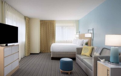 Sonesta ES Suites New Orleans double bed guest room, including large windows, sofa, and widescreen TV.