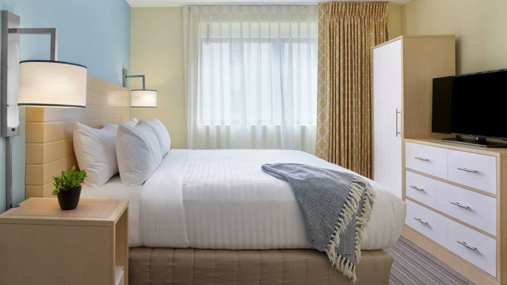 Double bed guest room in Sonesta ES Suites New Orleans, featuring bedside cabinet, widescreen TV, and large window.