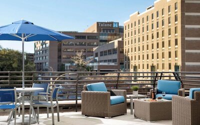 The rooftop terrace at Sonesta ES Suites New Orleans features armchairs and coffee tables, plus shaded tables and chairs, amid the fresh air.
