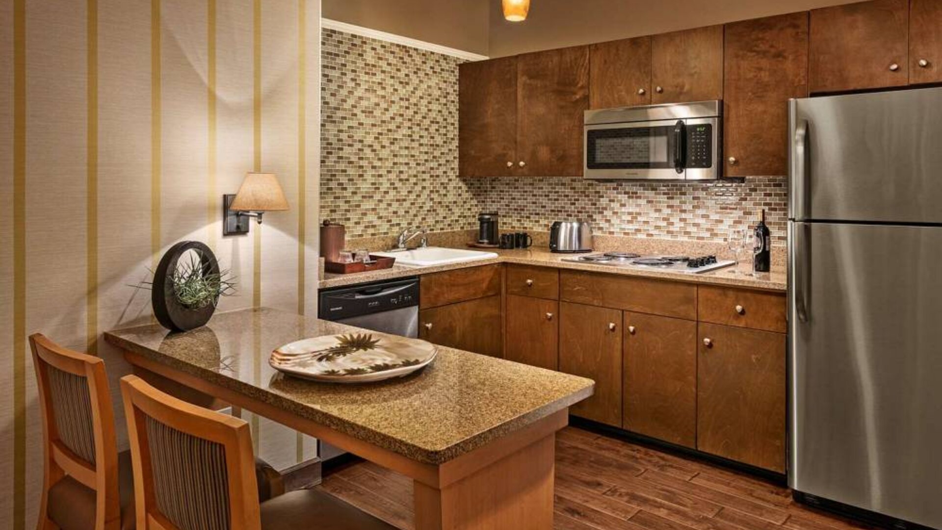 Sonesta Suites Scottsdale Gainey Ranch guest room kitchen, including table and two stools, oven and hob, microwave, and fridge-freezer.
