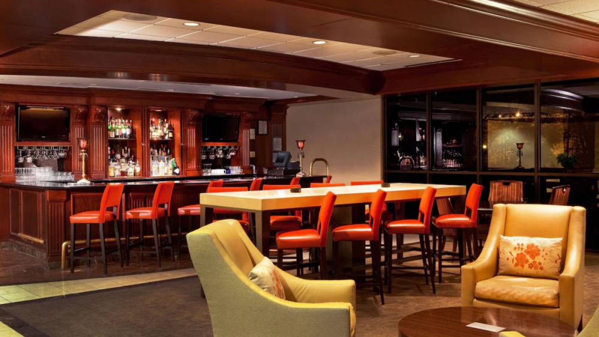 The hotel’s lobby lounge includes armchairs surrounding a coffee table, plus a bar with tall red stools and assorted refreshments.