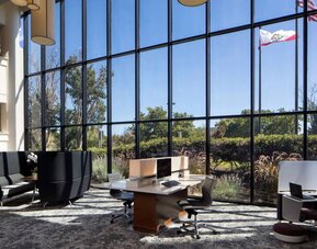 The hotel’s business center has a wall of windows next to it with a view of greenery and flags, while the center itself features multiple workstations and nooks for guests to use.