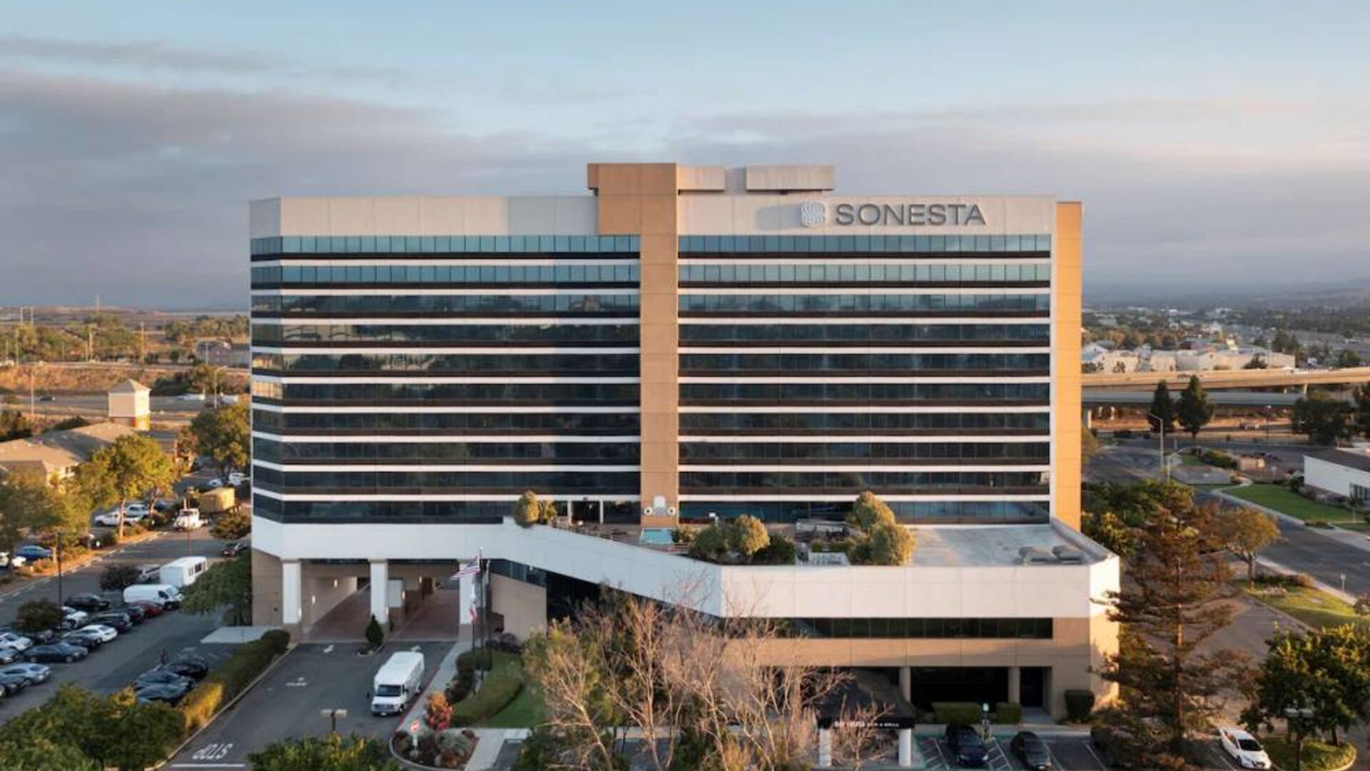 Sonesta San Jose’s exterior has ample parking for guests, abundant greenery, and a pool, plus the hotel chain’s name on the outside of the top floor.