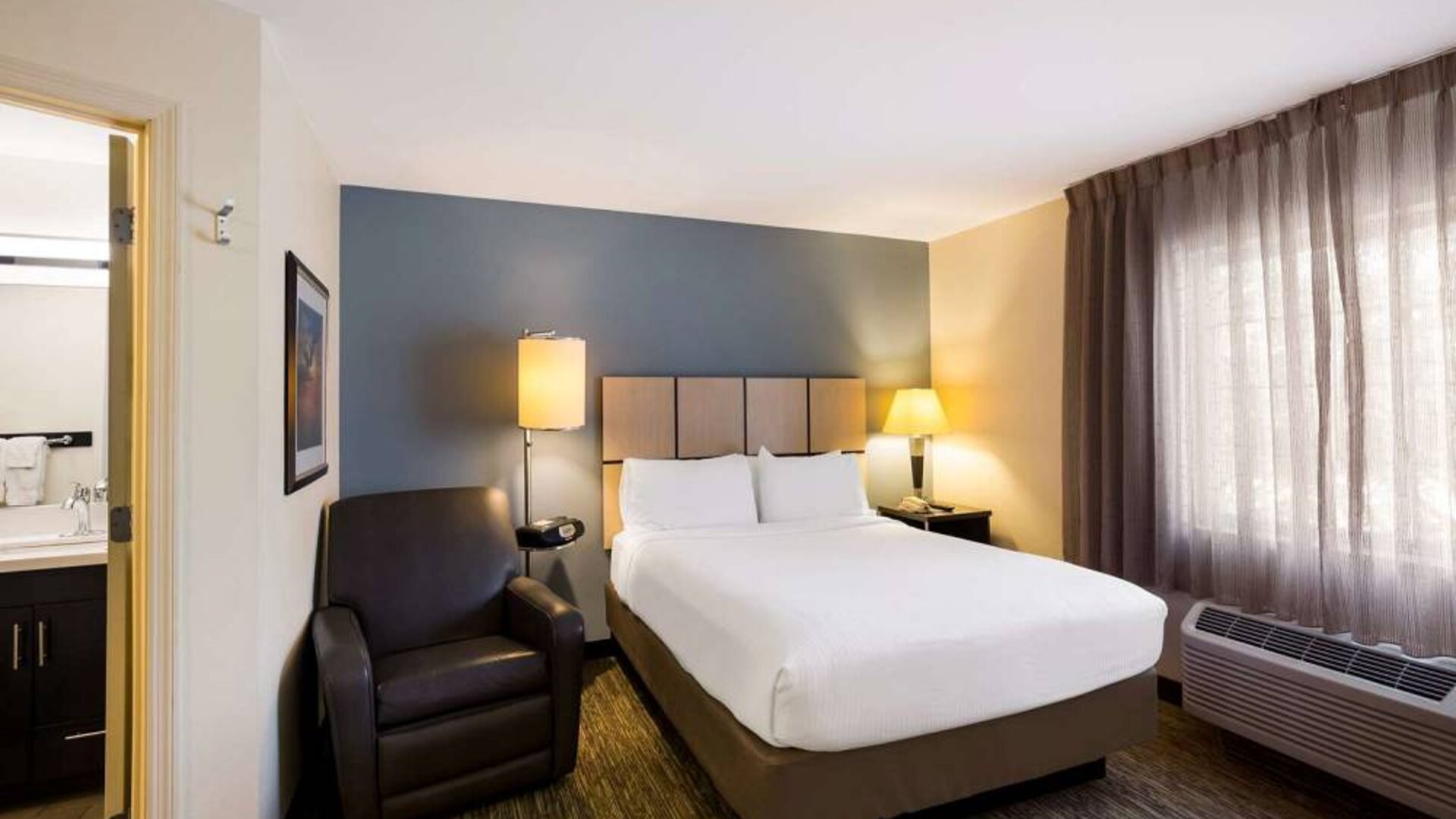 Sonesta Simply Suites St Louis Earth City double bed guest room, featuring armchair, window, and ensuite bathroom.