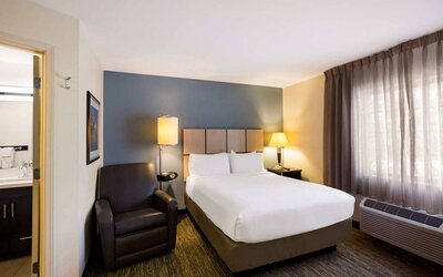 Sonesta Simply Suites St Louis Earth City double bed guest room, featuring armchair, window, and ensuite bathroom.