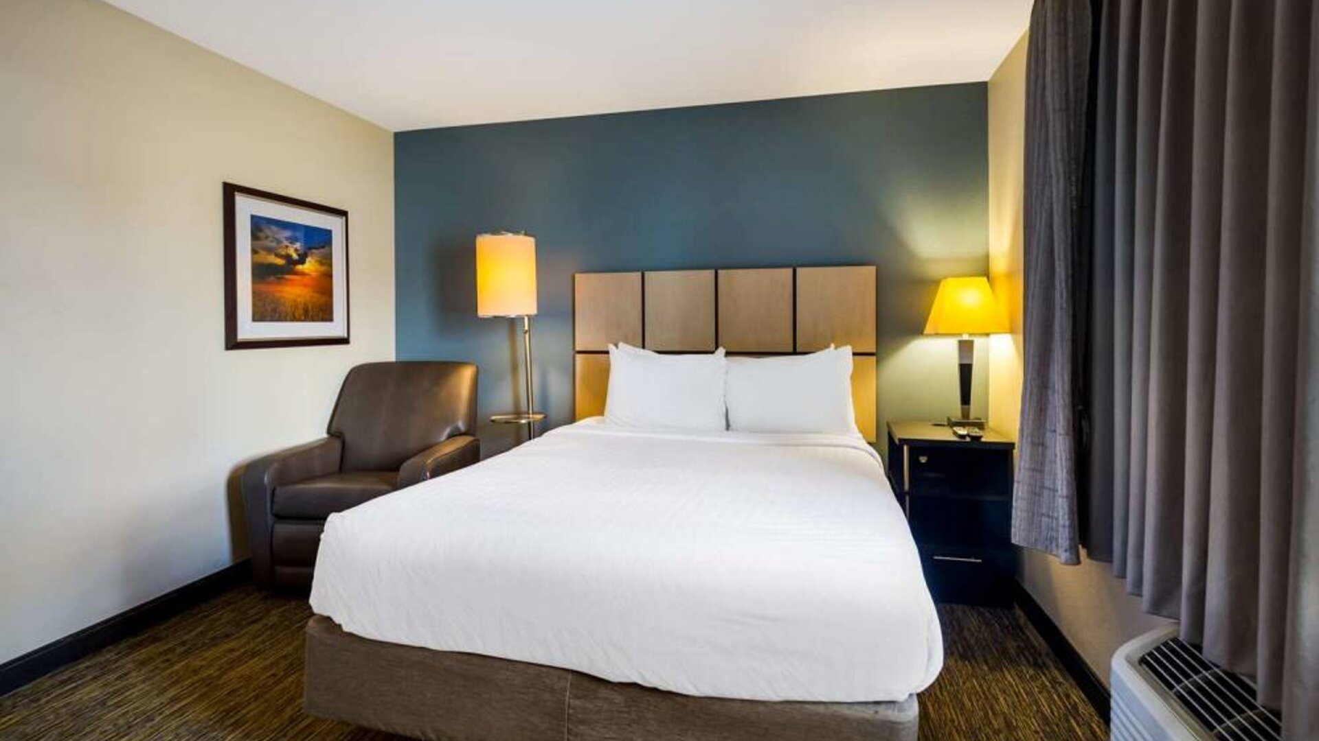 Sonesta Simply Suites St Louis Earth City double bed guest room, featuring bedside lamps, window, and armchair.