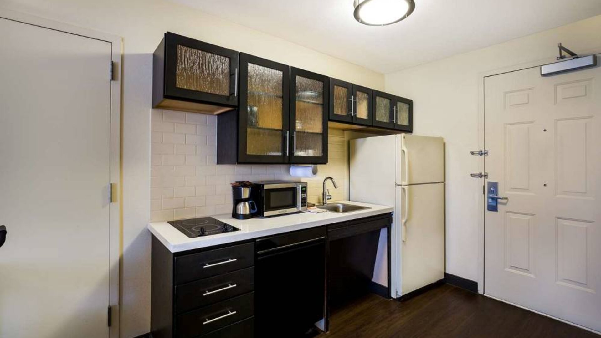 Sonesta Simply Suites St Louis Earth City guest room kitchen, complete with array of cupboards and drawers, plus a hob, microwave, and fridge-freezer.