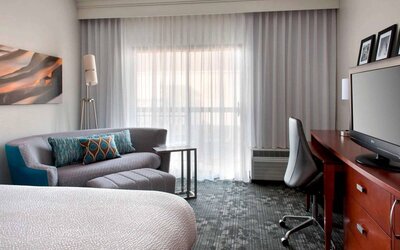 Double bed guest room in Sonesta Select Newport Middletown, featuring sofa, chair, window, and TV.