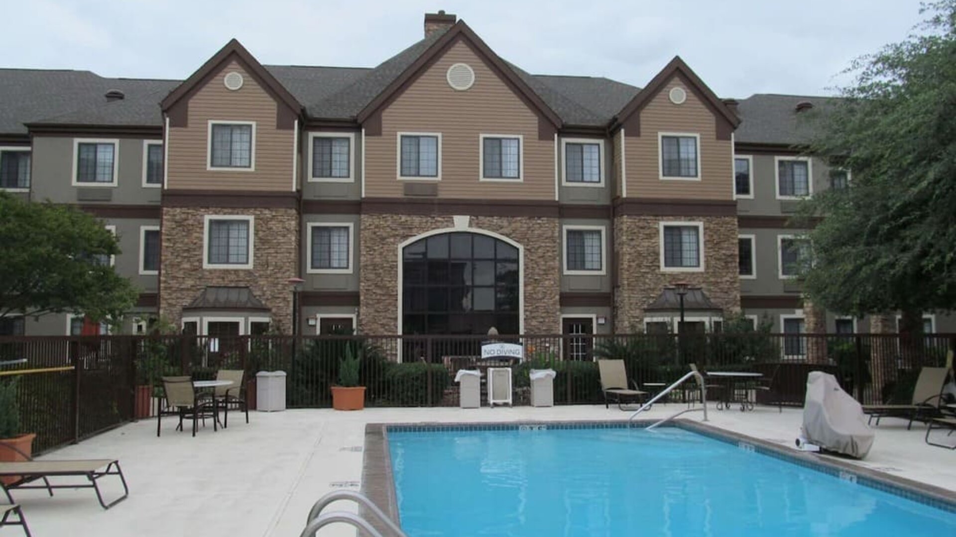 Sonesta ES Suites San Antonio Northwest - Medical Center’s pool has both sun loungers, and tables and chairs nearby, plus potted plants and more greenery beyond the fence.