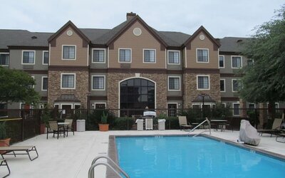Sonesta ES Suites San Antonio Northwest - Medical Center’s pool has both sun loungers, and tables and chairs nearby, plus potted plants and more greenery beyond the fence.