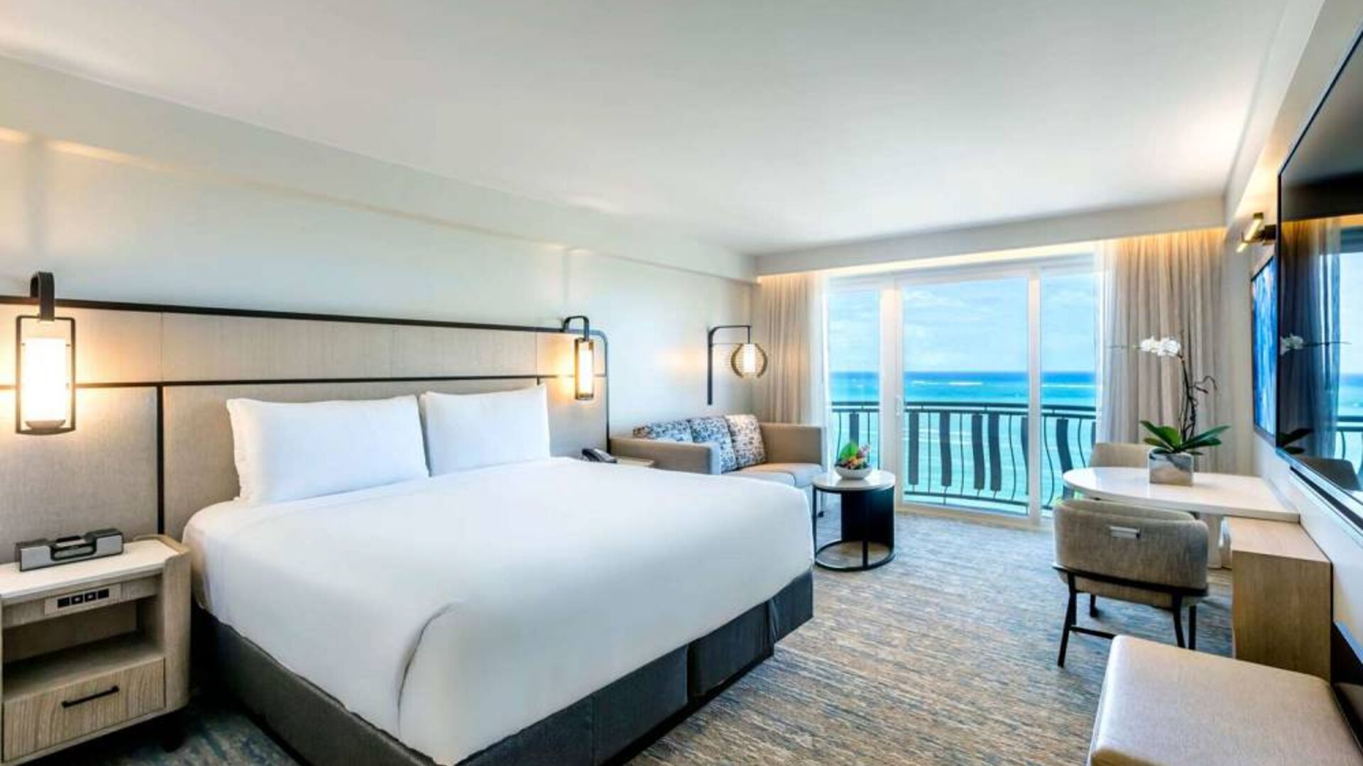 Royal Sonesta San Juan double bed guest room, furnished with table and chairs, sofa and coffee table, and a a balcony with ocean views.