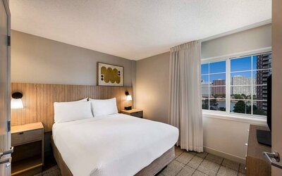 Double bed guest room in Sonesta Simply Suites Jersey City, including art on the wall, TV, and window.