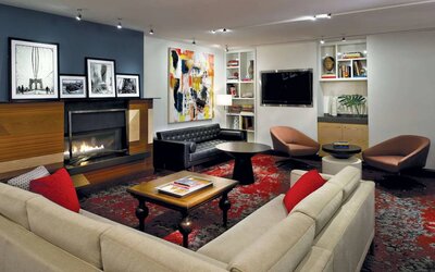 The Den’s lounge in The Fifty Sonesta Select New York features armchairs and sofas, coffee tables and a fireplace, plus a large TV.