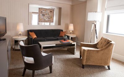 The Benjamin Royal Sonesta New York guest room living area, furnished with coffee table, chairs, TV, and sofa.