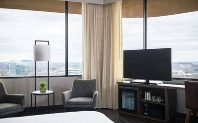 Sonesta Nashville Airport guest room, featuring widescreen television, chairs and a coffee table, and large windows.