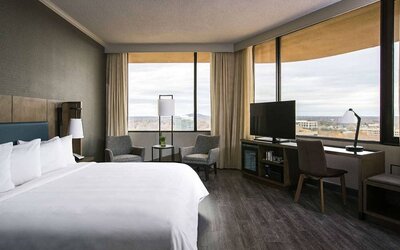 Double bed guest room in Sonesta Nashville Airport, furnished with chairs, coffee table, TV, large windows, and a workspace desk and chair.