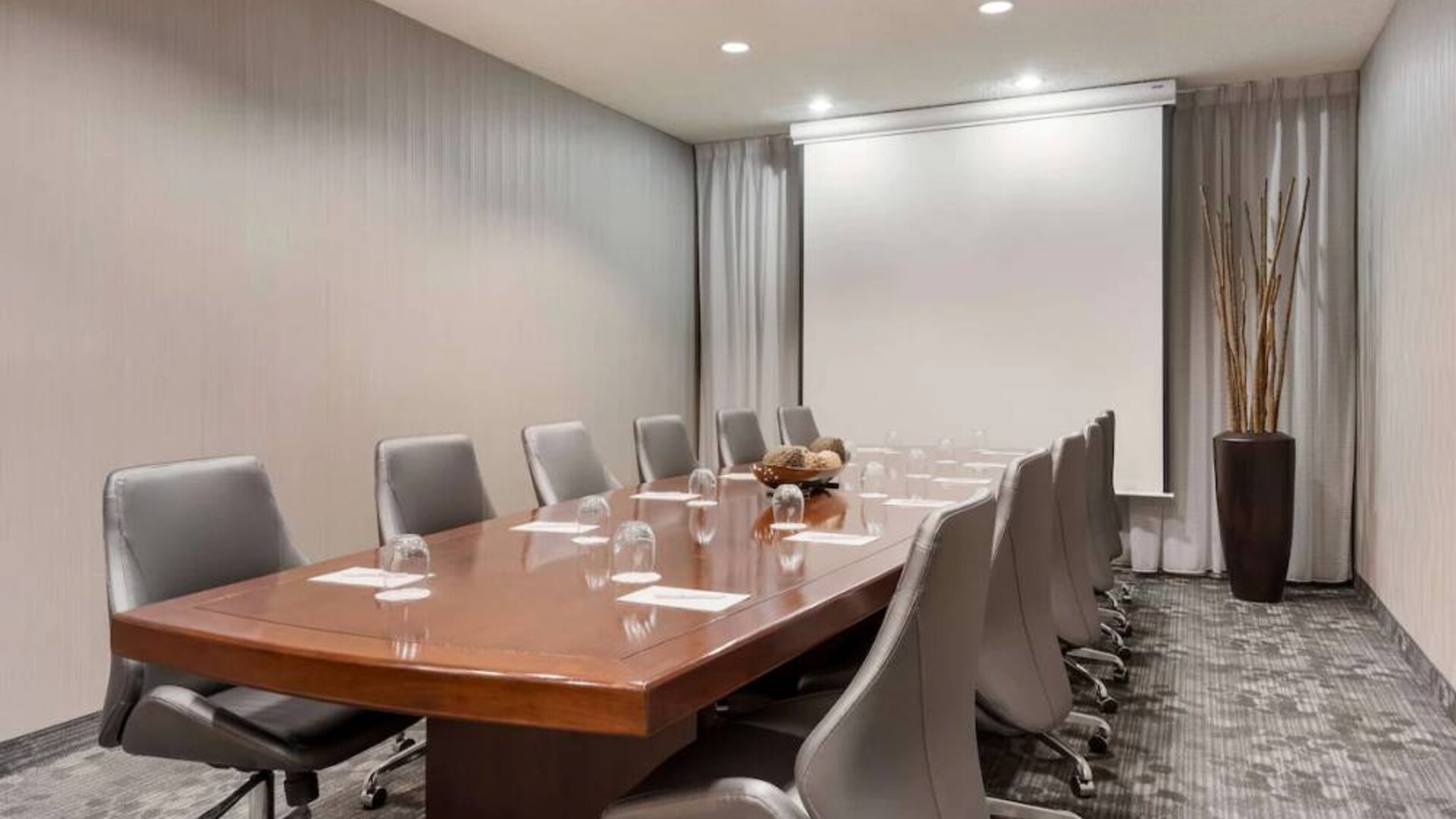Sonesta Select Tempe Downtown meeting room, featuring long wooden table, a dozen swivel chairs, and a projector screen.