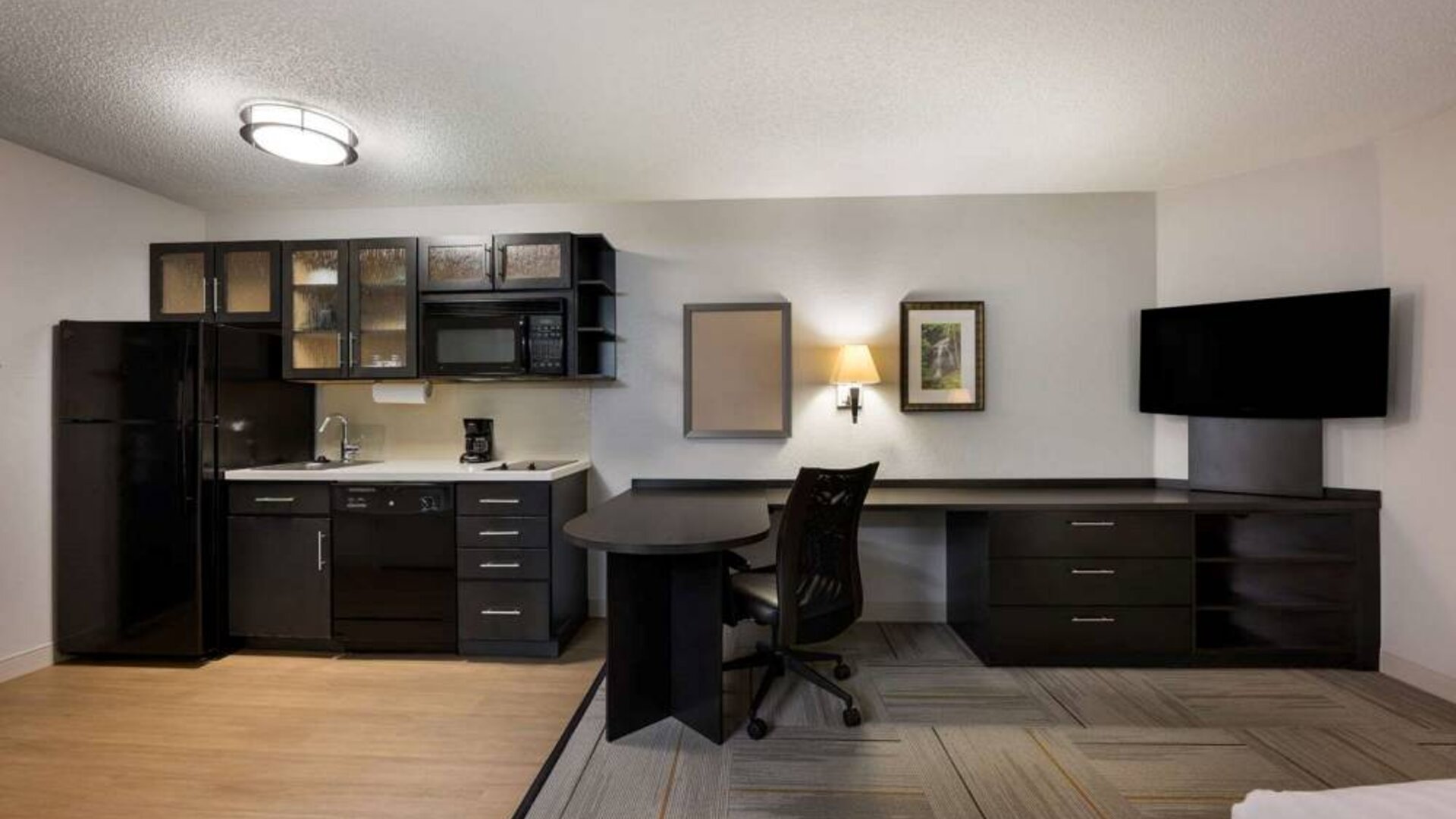 Sonesta Simply Suites Huntsville Research Park guest room, featuring TV and kitchen, between which is a workspace desk and chair.
