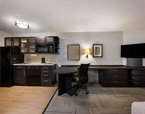 Sonesta Simply Suites Huntsville Research Park guest room, featuring TV and kitchen, between which is a workspace desk and chair.