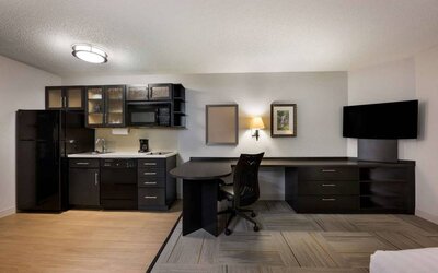 Sonesta Simply Suites Huntsville Research Park guest room, featuring TV and kitchen, between which is a workspace desk and chair.
