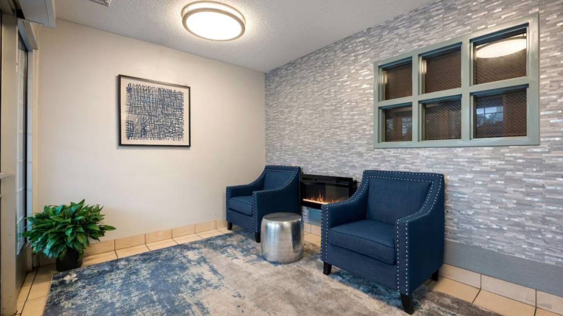 The hotel lobby has a pair of blue armchairs with a fireplace and coffee between them, and a potted plant in the corner.