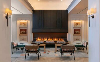 The lobby lounge of Royal Sonesta Chicago Downtown is furnished with comfortable seats and coffee tables close to a fireplace, with art on the walls.
