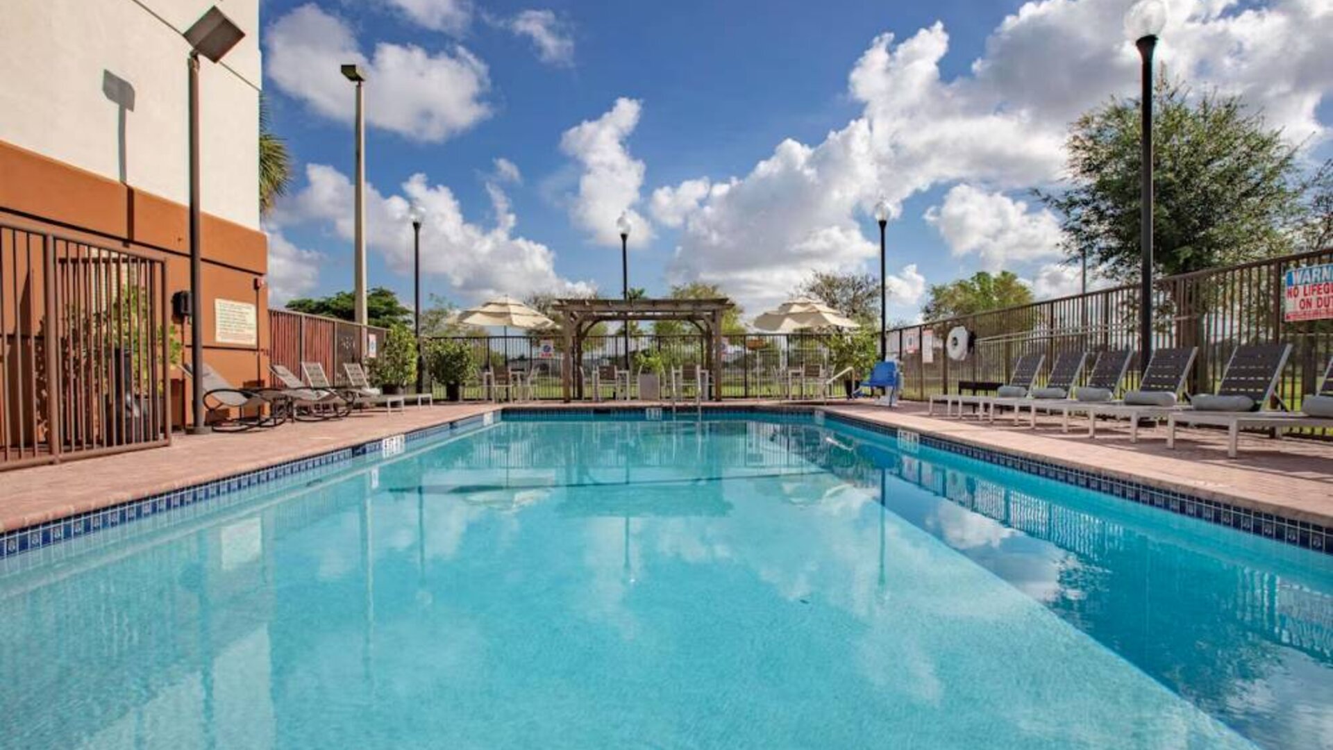 Sonesta Simply Suites Miami Airport Doral’s outdoor pool has sun loungers by the side, and tables and chairs nearby.