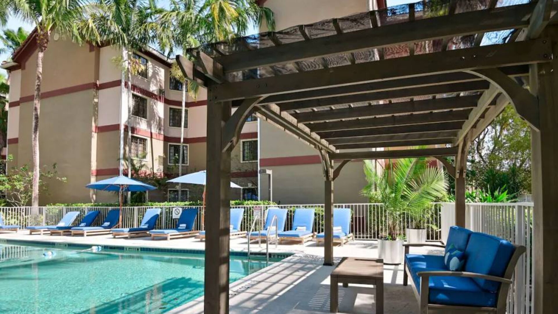 Sonesta ES Suites Fort Lauderdale Plantation’s outdoor pool has sofa seating and a coffee table by the side, alongside a row of sun loungers.