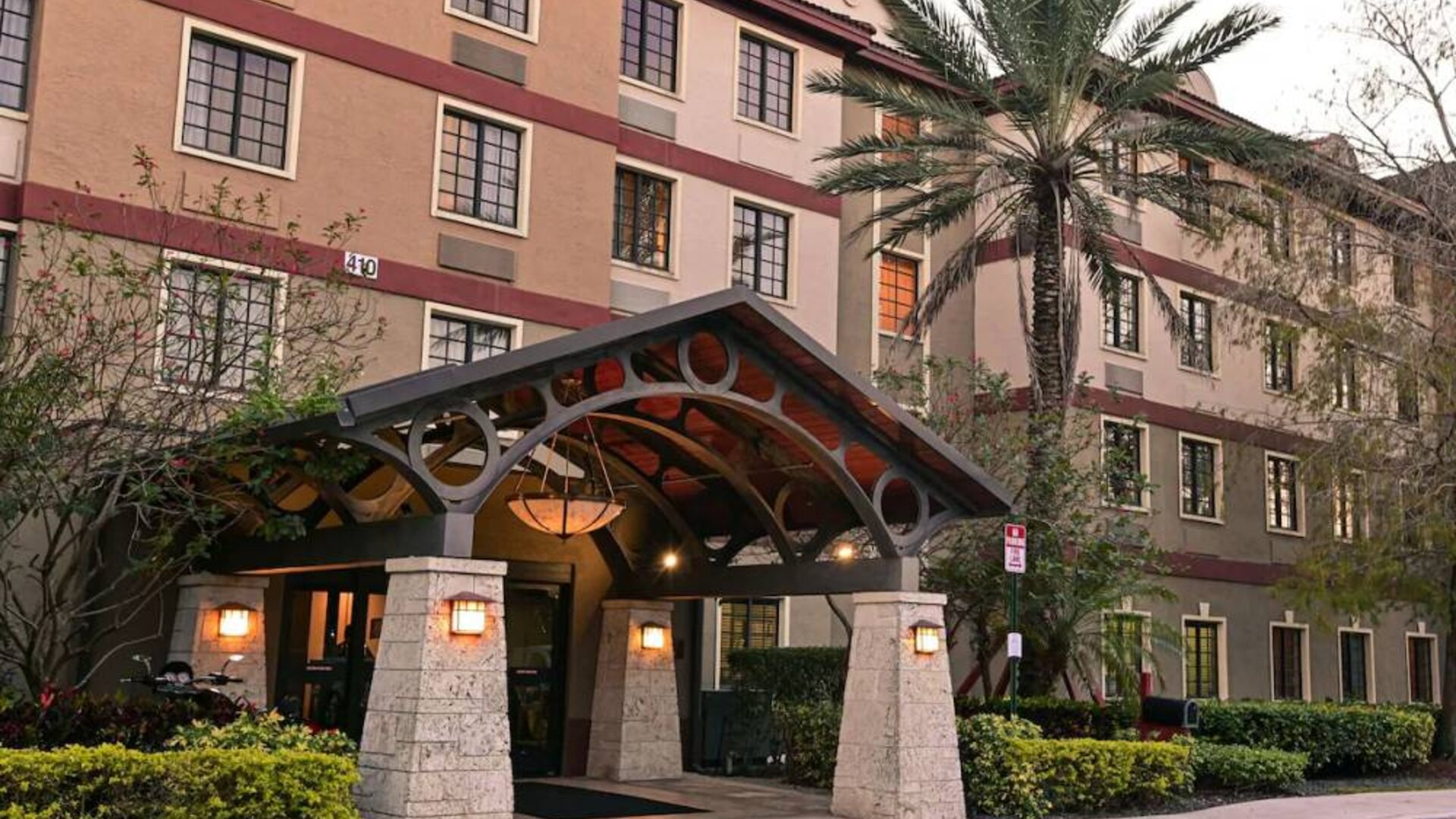 The hotel’s exterior features a covered entrance beside which there’s extensive greenery, including a towering palm tree.