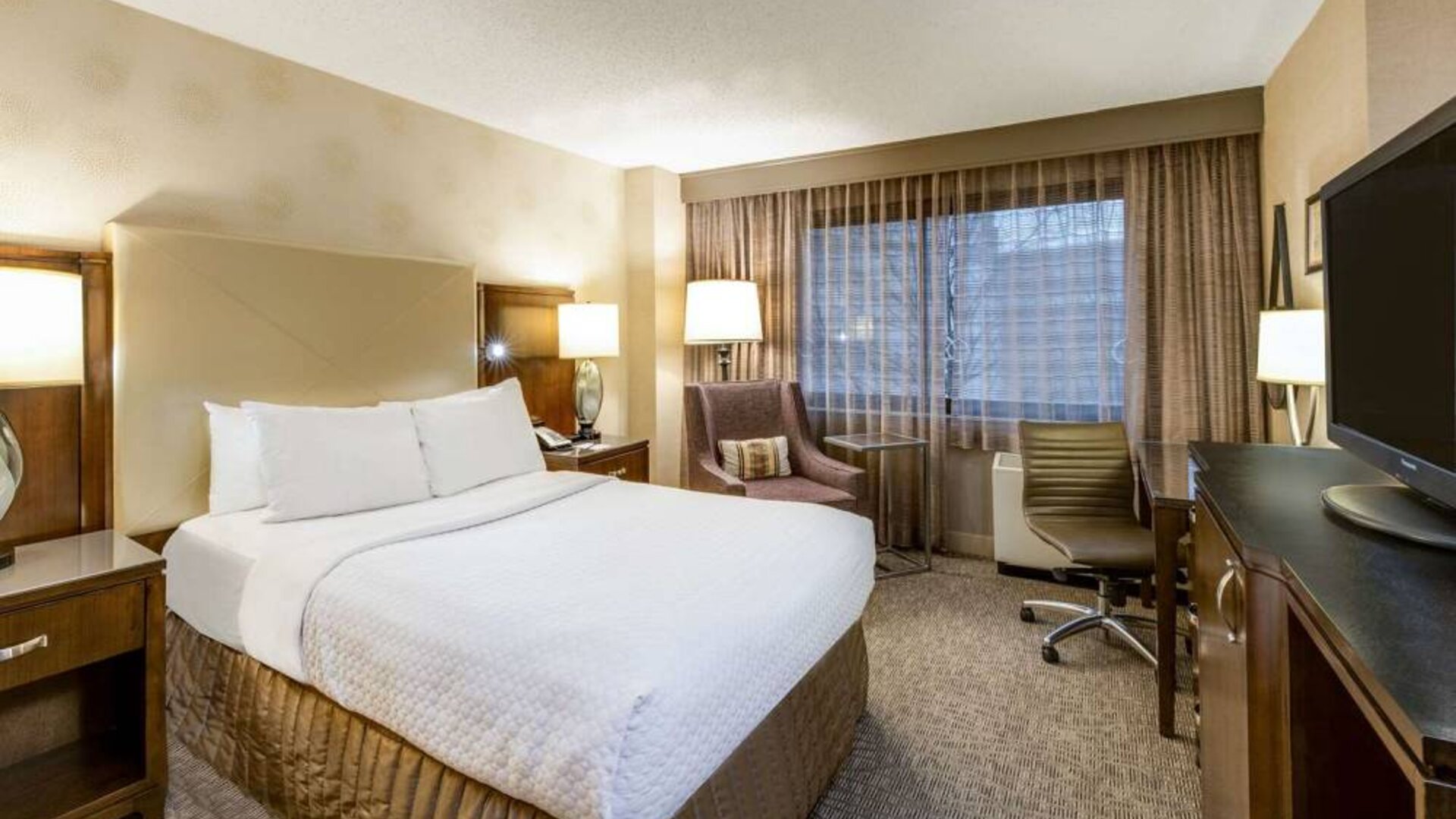 Sonesta White Plains Downtown double bed guest room, with armchair, TV, desk and chair, and a window.