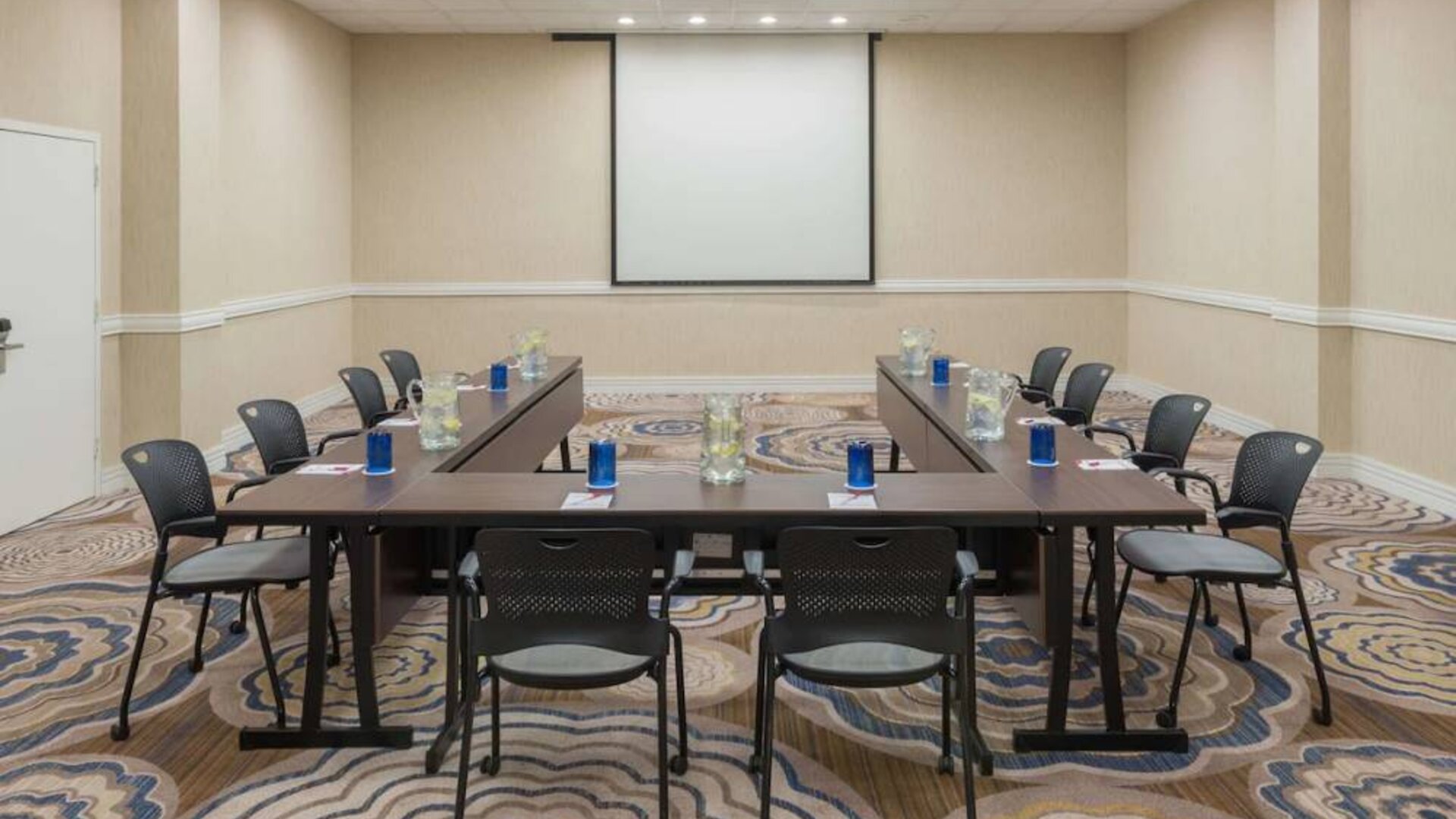 Meeting room in Sonesta White Plains Downtown, with tables arranged in a U-shape, seating for 10, and a projector screen.