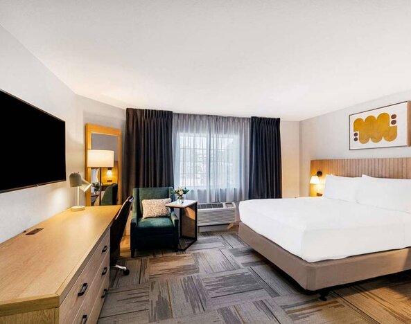 Double bed guest room in Sonesta Simply Suites Austin South, including window, armchair, and a widescreen television.