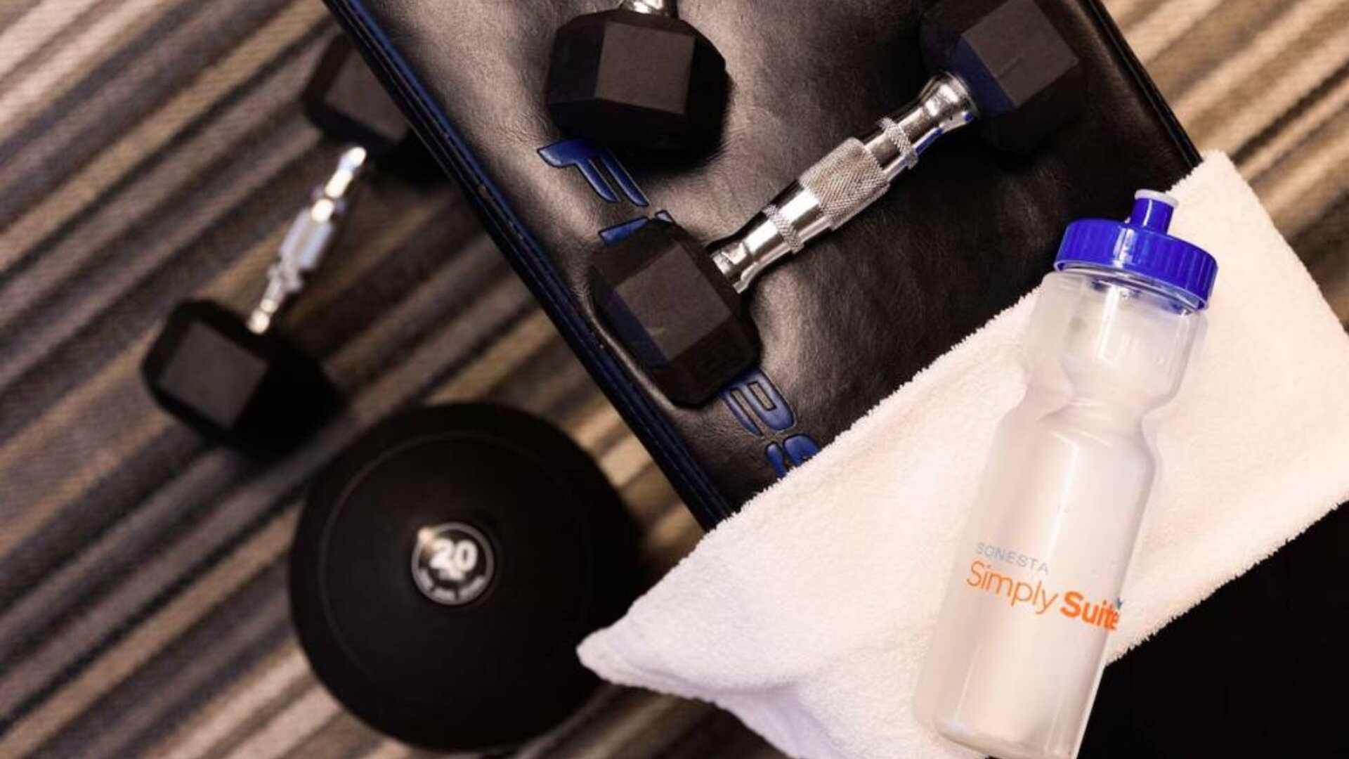 The fitness center at Sonesta Simply Suites Plano Frisco includes free weights and benches for guests to use, plus towels and water.