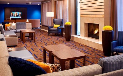 Sonesta Select Detroit Auburn Hills’ lobby lounge is furnished with sofas, armchairs, coffee tables, a fireplace and a wall-mounted TV.