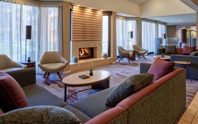 The lobby lounge in Sonesta Select Indianapolis Carmel has a mix of comfy chairs and large sofas, plus coffee tables and a fireplace.
