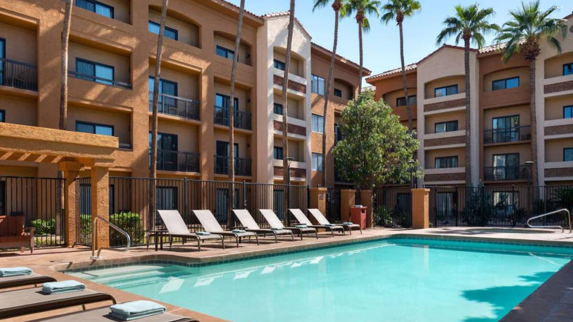 Sonesta Select Phoenix Camelback’s outdoor pool has sun loungers by the side, a shaded area, and tall palm trees.