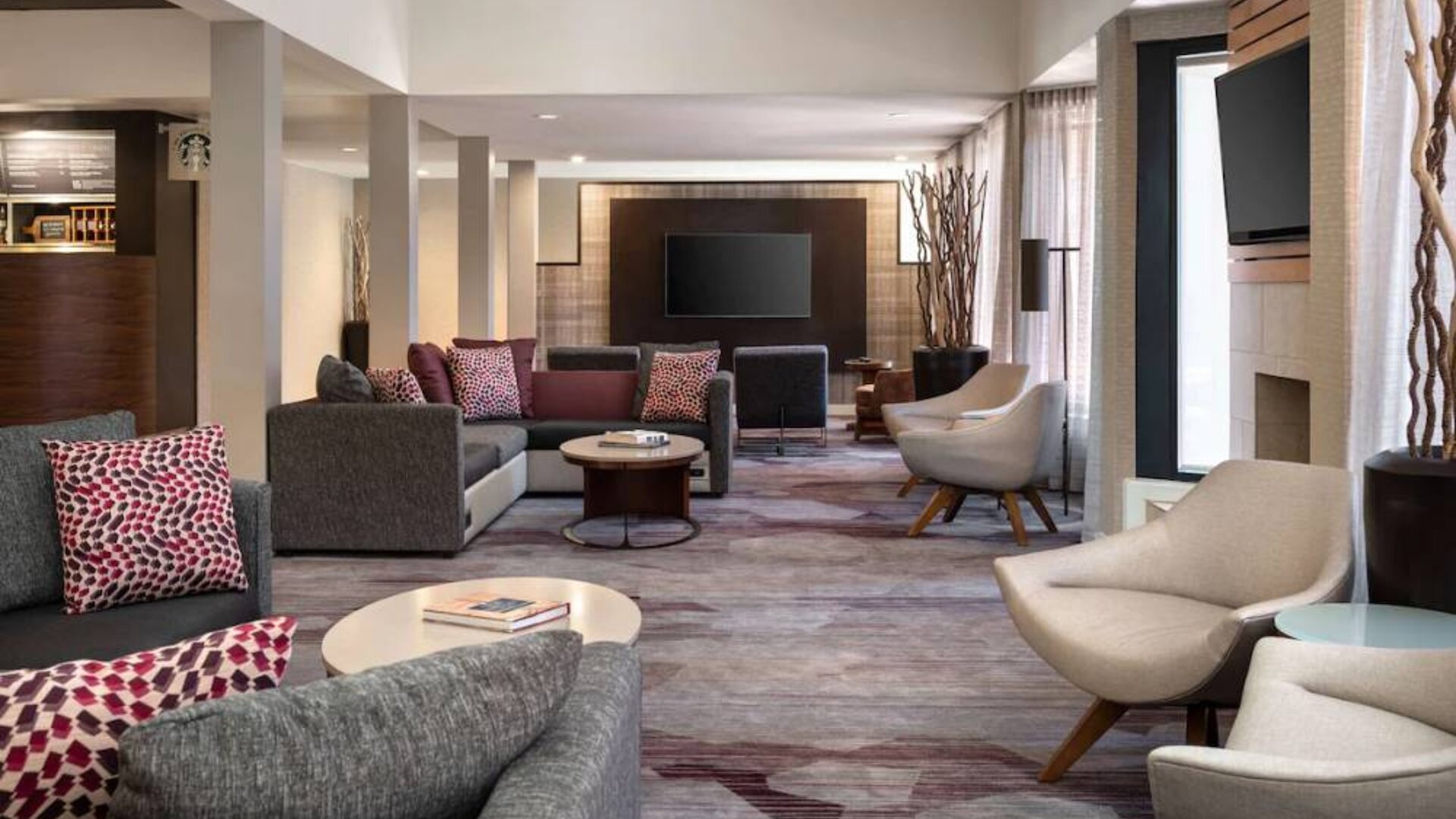 Lounge in the hotel lobby, furnished with comfy chairs and large sofas, coffee tables and multiple large televisions.