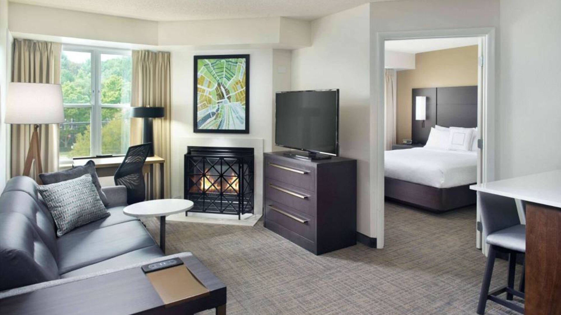 Sonesta ES Suites Raleigh Cary double bed guest room, with a living area furnished with sofa, coffee table, fireplace, and TV.