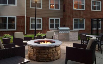 The fire pit at Sonesta ES Suites Raleigh Cary has armchairs around it, a barbecue, and potted plants.