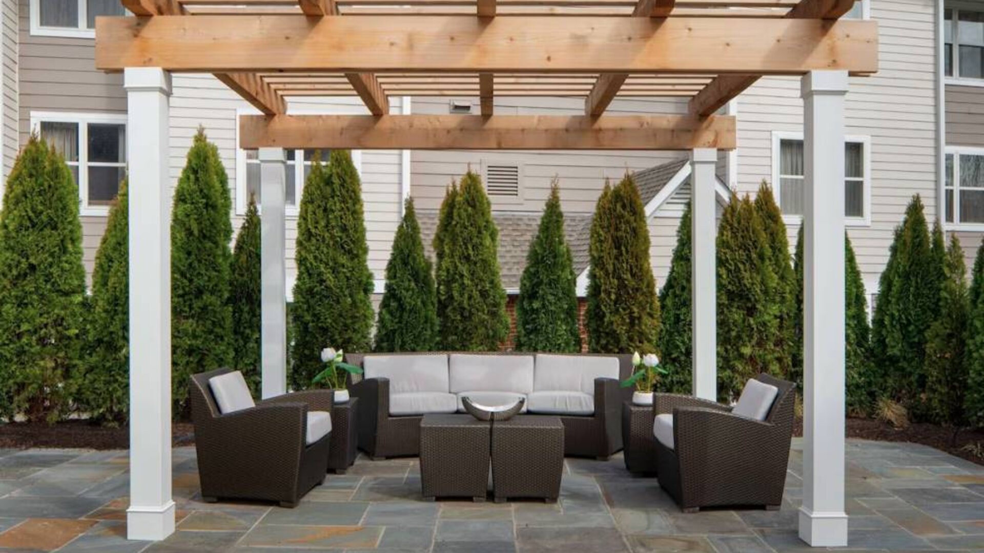 Sonesta ES Suites Fairfax Fair Lakes’s patio is furnished with armchair and sofa seating, plus coffee tables and nearby greenery.