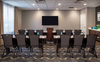 Hotel meeting room, with tables and twelve seats facing a lectern and wall-mounted TV.