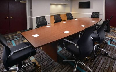 Hotel meeting room, with long wooden table, eight swivel chairs, and a wall-mounted television.