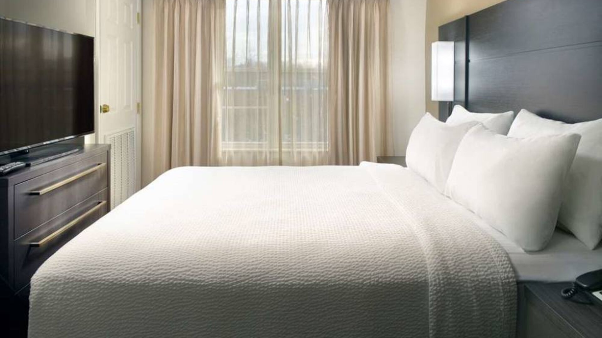 Double bed guest room with a window and large TV at Sonesta ES Suites Raleigh Durham Airport Morrisville.