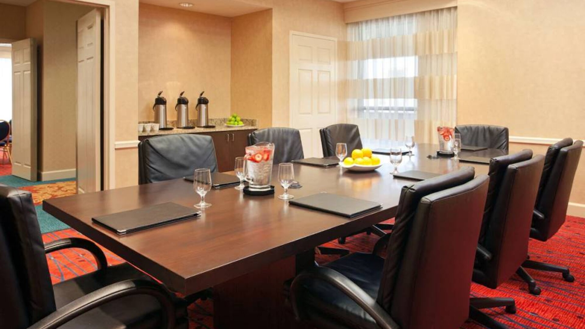 Hotel meeting room with long wooden table, large window, and eight leather chairs.