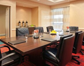 Hotel meeting room with long wooden table, large window, and eight leather chairs.