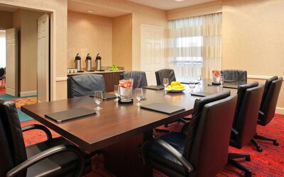 Hotel meeting room with long wooden table, large window, and eight leather chairs.
