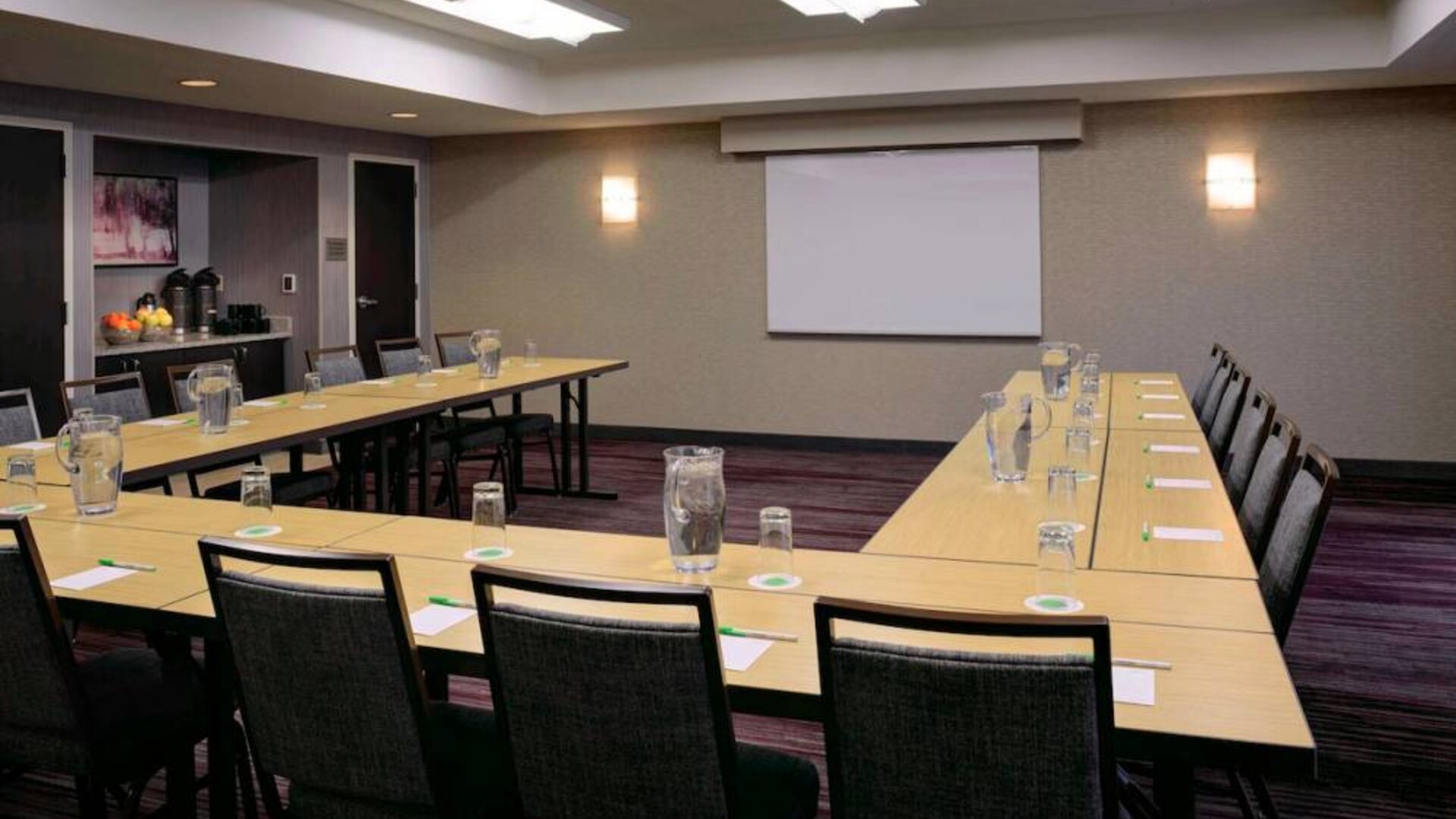 Hotel meeting room with a projector screen and tables arranged in a U-shape.