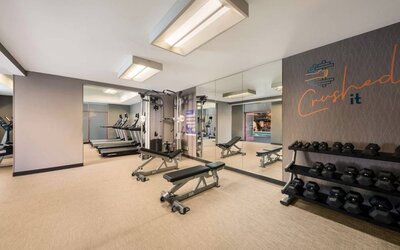 Sonesta Select Pleasant Hill’s fitness center features free weights, a mirrored wall, and various exercise machines.