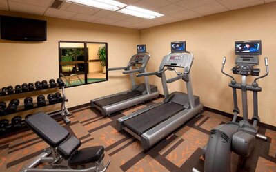 Sonesta Select Miami Lakes’ fitness center is equipped with various exercise machines, free weights, and a wall-mounted TV.