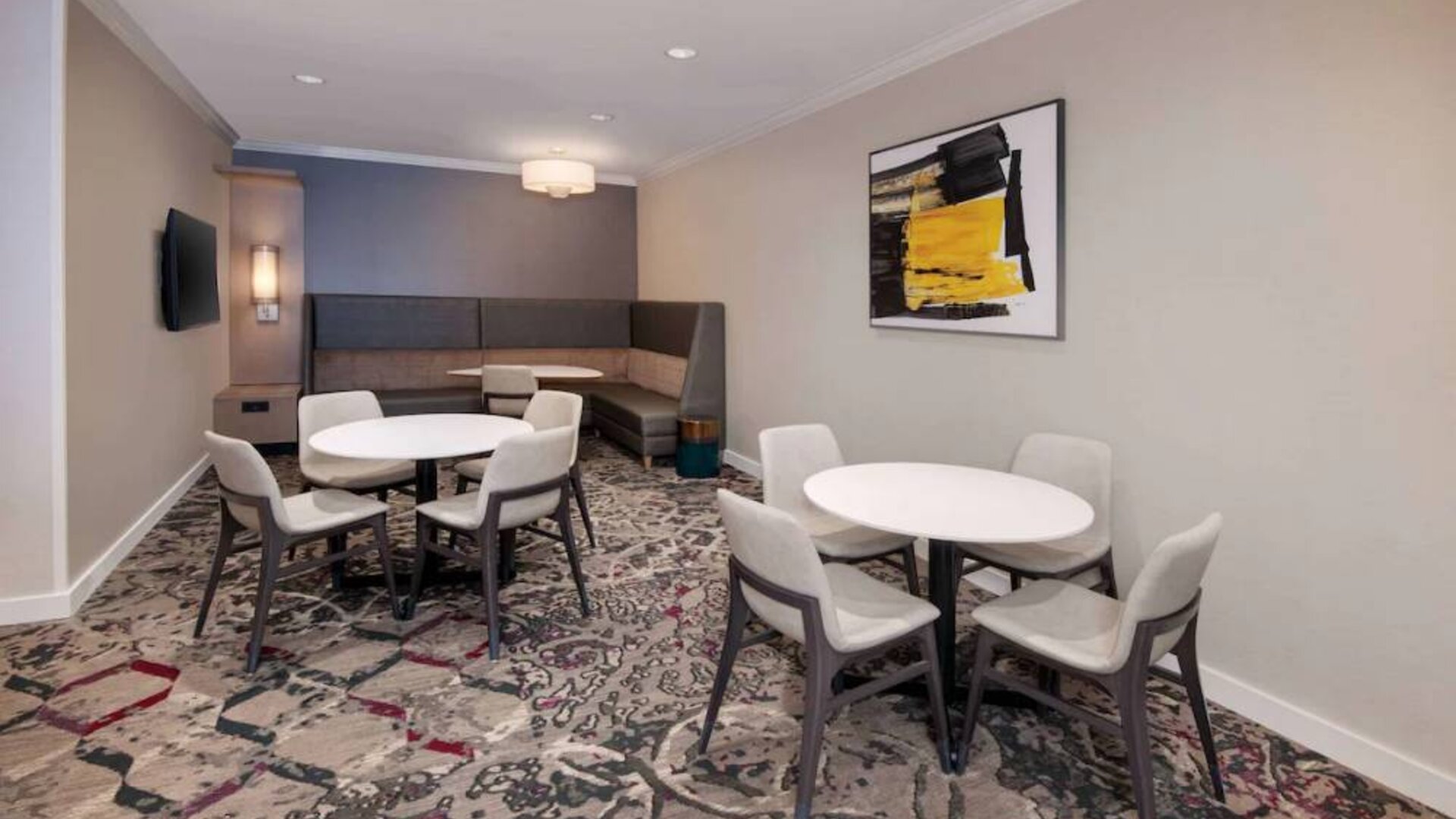 Lobby lounge in Sonesta ES Suites Atlanta Alpharetta North Point Mall with small tables and both art and a large TV on the wall.